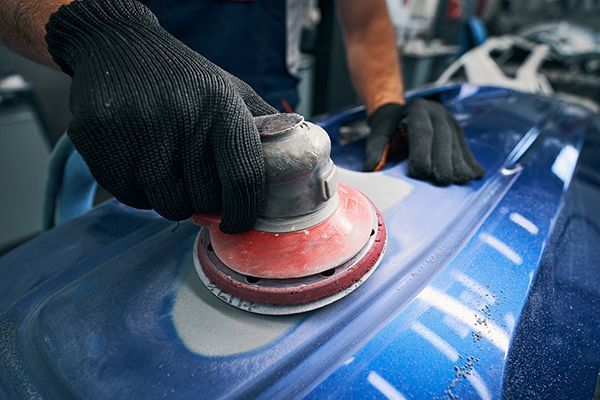 A man is sanding a blue car with an orbital sander.