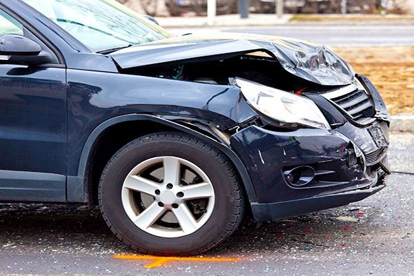 A car with a damaged front end is parked on the side of the road.