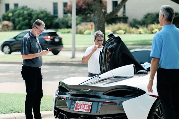 Three men are standing around a white sports car with the hood up.