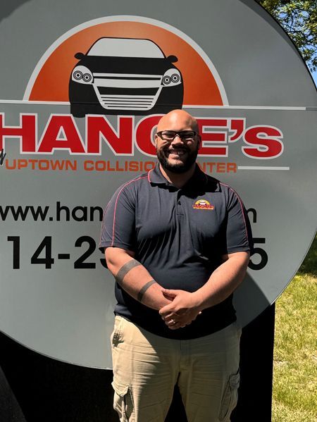 A man stands in front of a hange 's uptown collision center sign