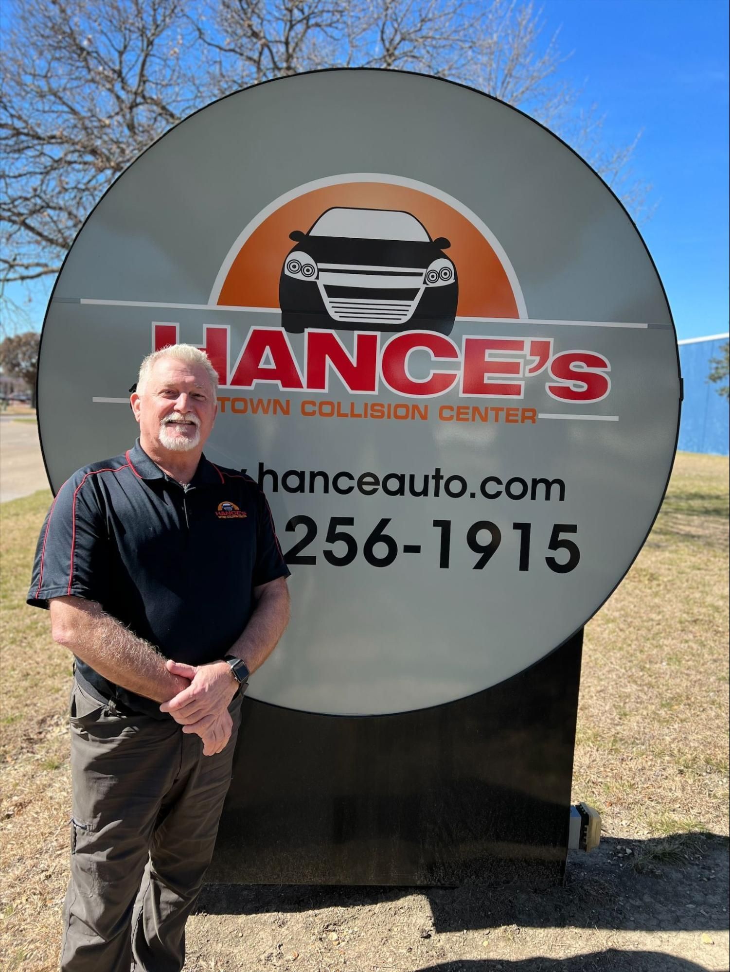 A man is standing in front of a sign for chance 's town collision center.