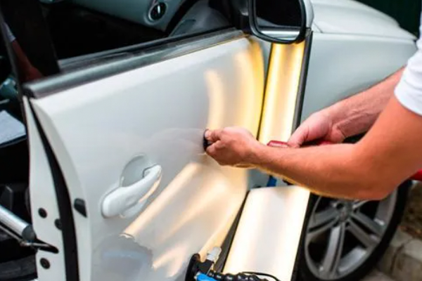 A man is repairing a car door with a light.
