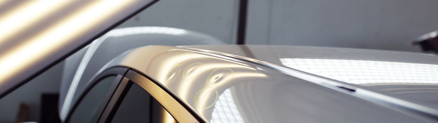 White car roof with multiple dents, being inspected under bright lighting.