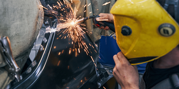A man wearing a yellow helmet is welding a piece of metal.