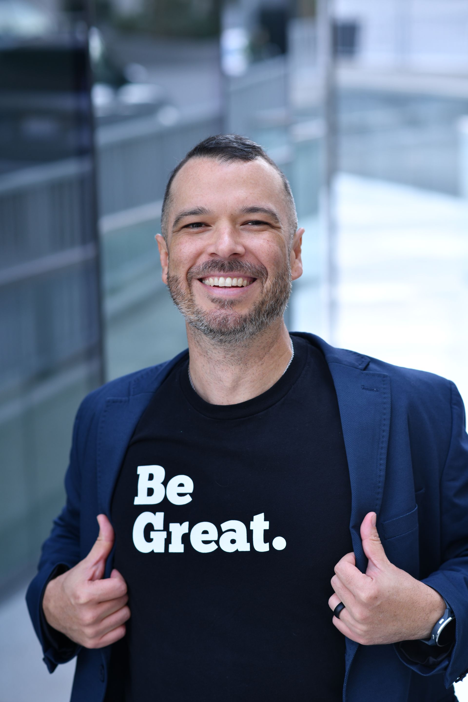 A man wearing a black shirt that says `` be great '' is giving a thumbs up.