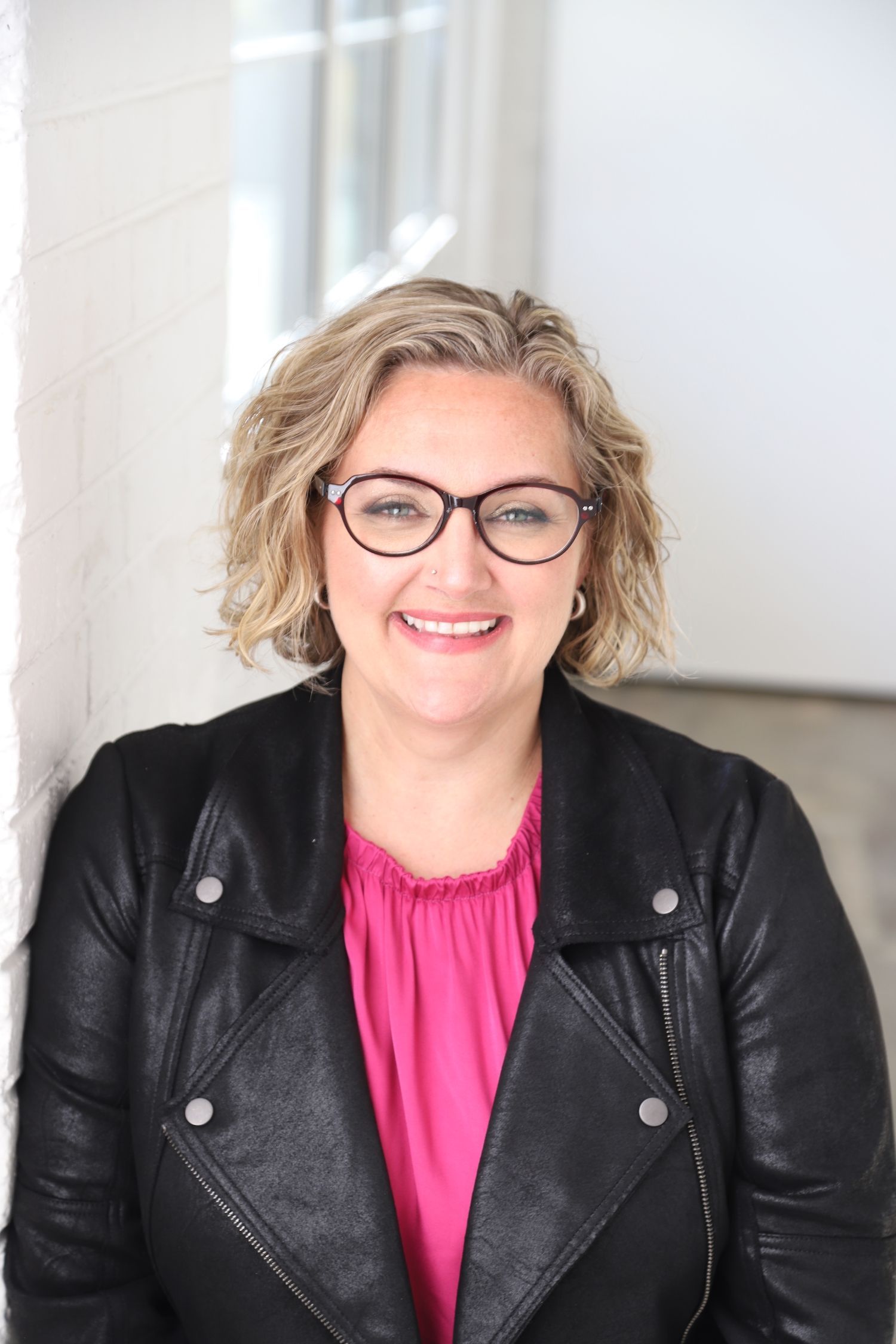 A woman wearing glasses and a leather jacket is smiling for the camera.