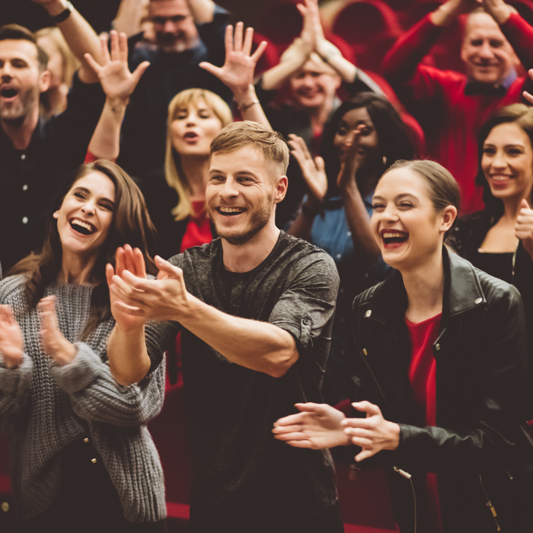 A group of people are clapping and laughing in a theater