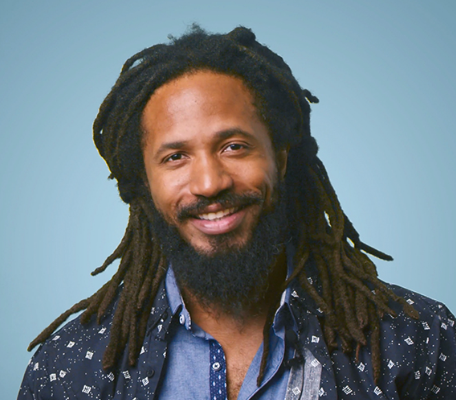 A man with dreadlocks and a beard is smiling for the camera.
