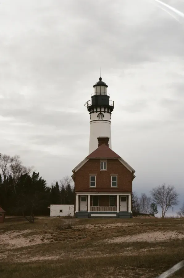 Film photograph of Au Sable Lighthouse with white tower and red brick building on a cloudy day.