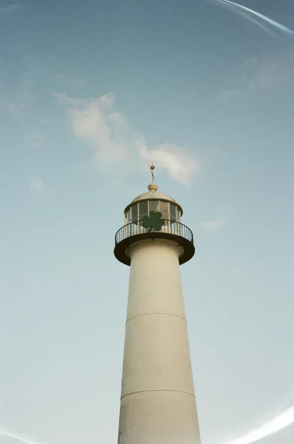 Film photograph of Biloxi Lighthouse with green shamrock against a pale blue sky.