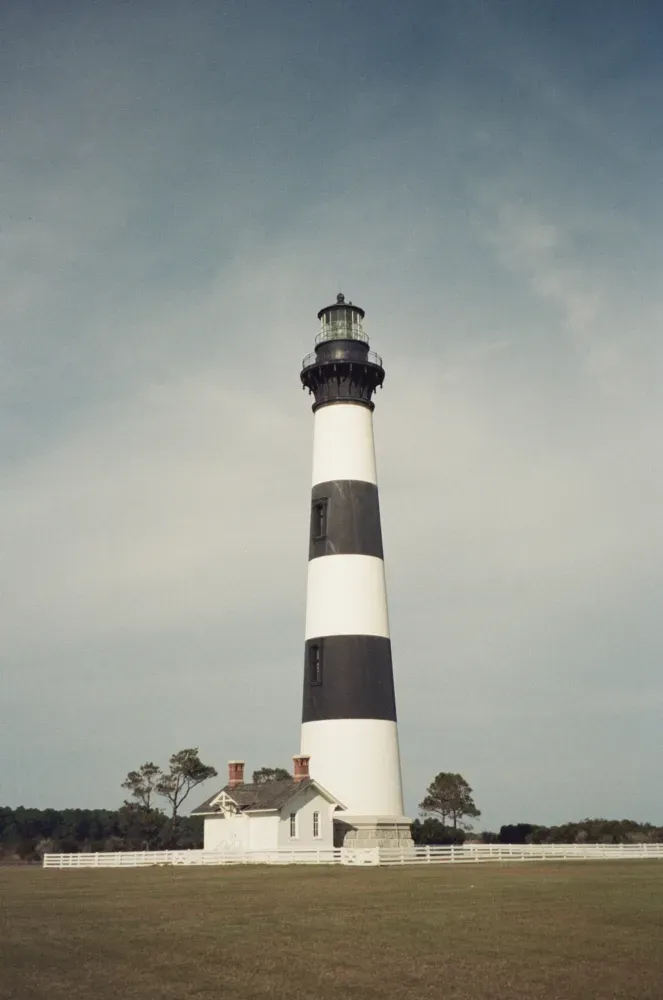 Black and white striped lighthouse on a grassy plain under a cloudy sky.