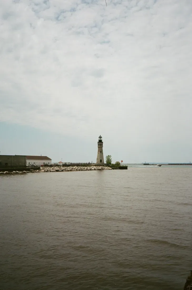 Buffalo Harbor lighthouse on a rocky breakwater by calm water under a cloudy sky