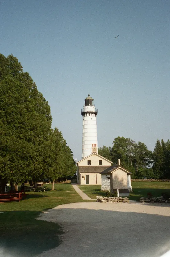 Cana Island lighthouse with attached building on a green lawn, under a blue sky.