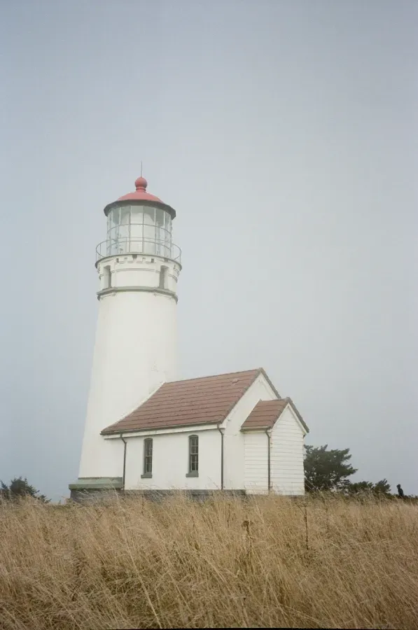 Film photograph of Cape Blanco lighthouse with red top and adjacent building in fog.