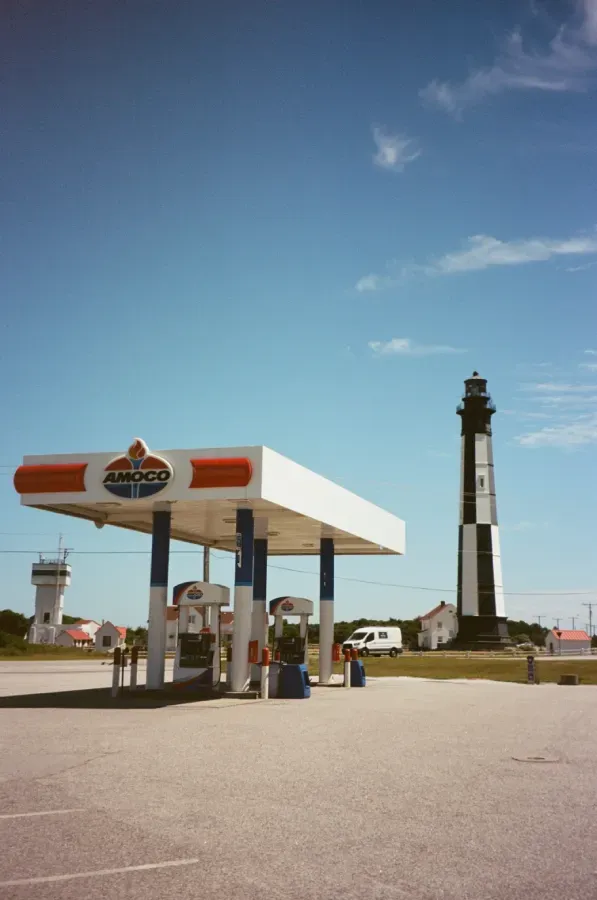 Gas station with AMOCO sign next to the Cape Charles lighthouse under a blue sky.