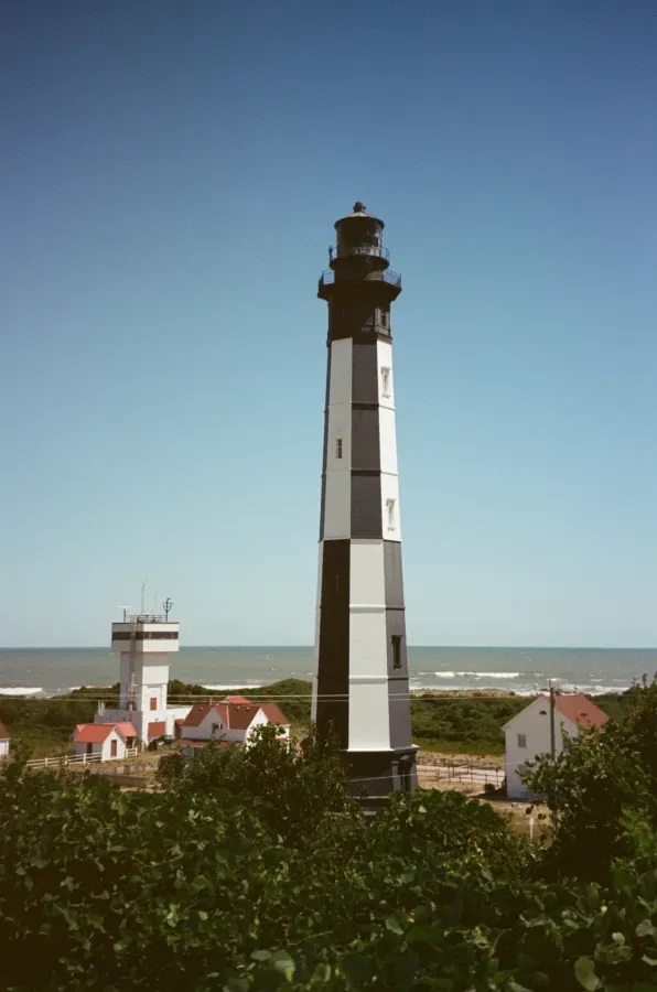 The Cape Charles lighthouse on coast, with small buildings and ocean visible.