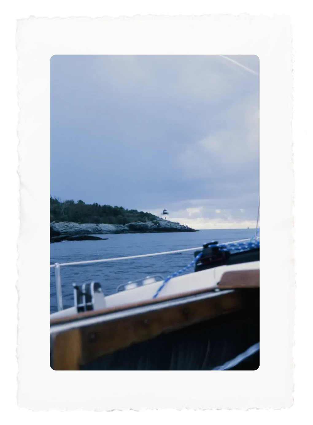 View from a boat of a calm blue sea, cloudy sky, and tree-lined shoreline