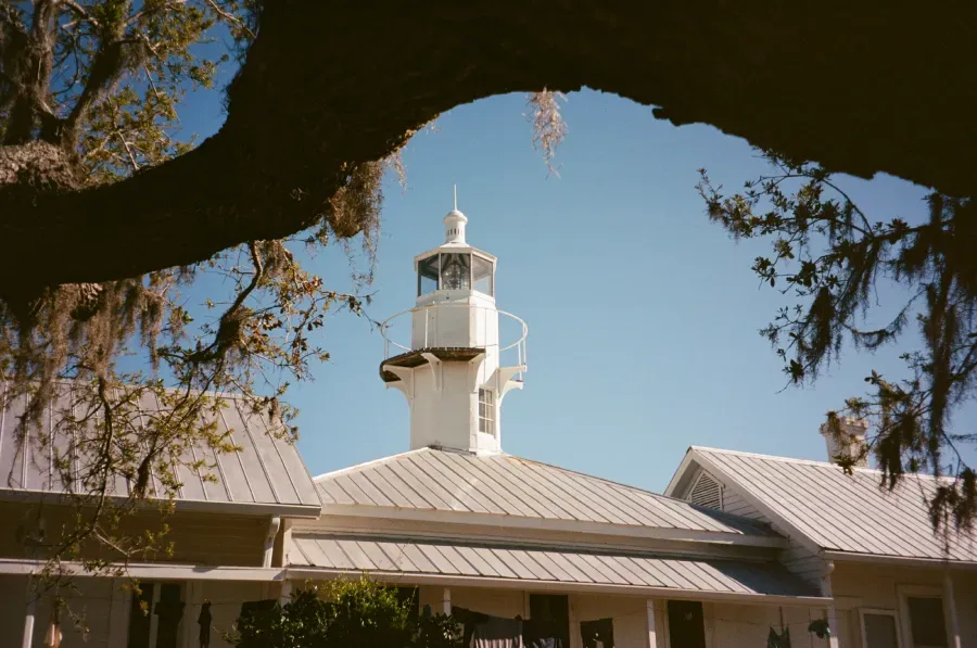 Cedar Key lighthouse atop building, framed by tree branches, against a clear blue sky.