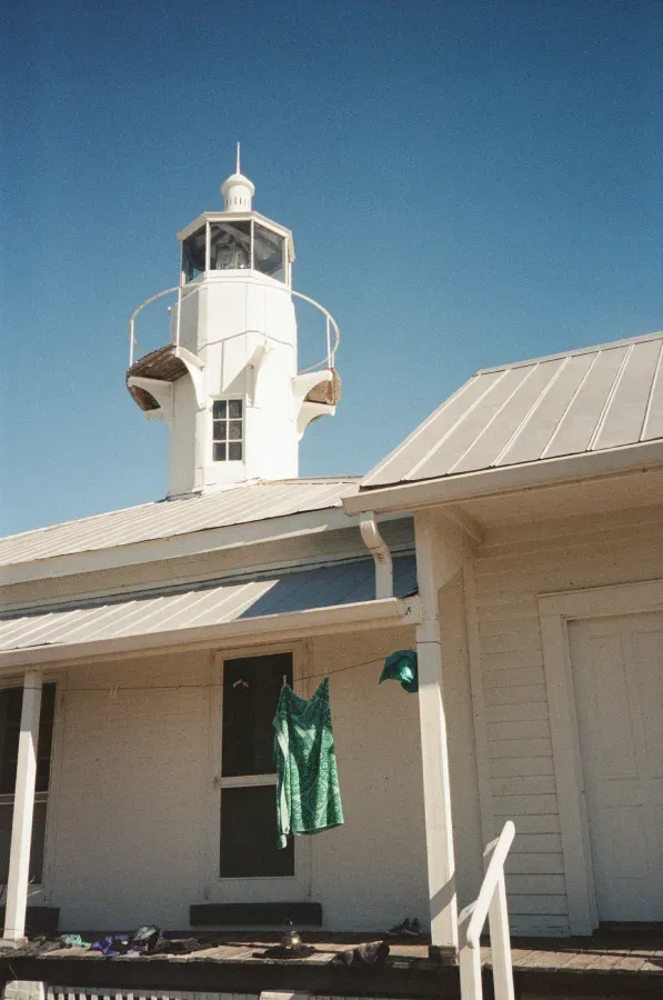 Cedar Key lighthouse with spiral staircase against a bright blue sky. Green dress hangs on a clothesline.
