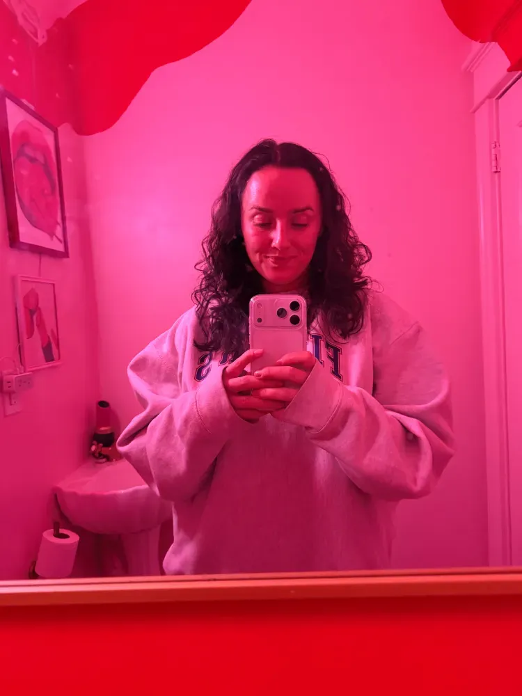 Charlee Remitz takes a mirror selfie in a room bathed in vibrant pink light.