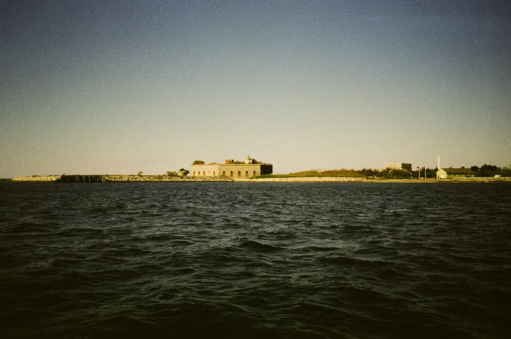 Distant photo of Clark's point lighthouse on a calm sea under a clear sky at sunset