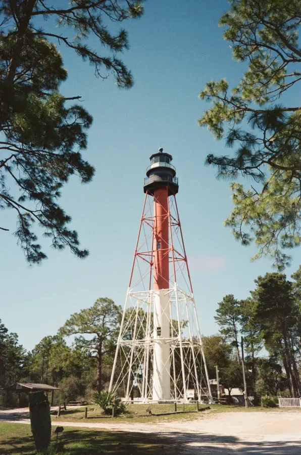 Red and white Crooked River lighthouse, surrounded by trees, under a blue sky.