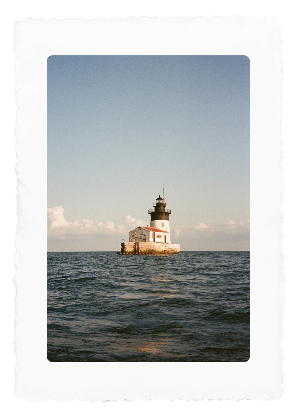 Lighthouse on a small rocky islet in a calm blue sea under a clear sky