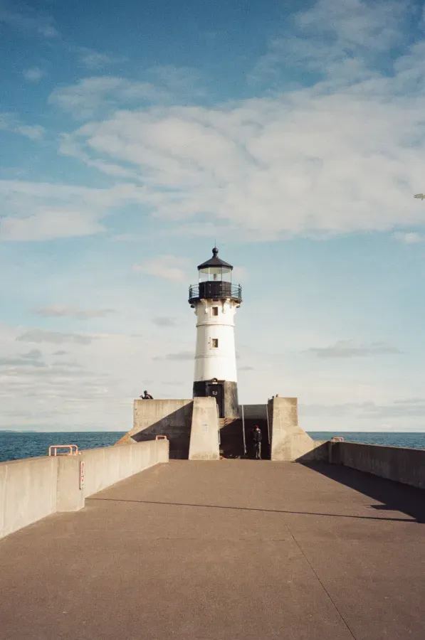 Duluth Harbor Lighthouse on a concrete pier, black and white structure under a blue sky with clouds.