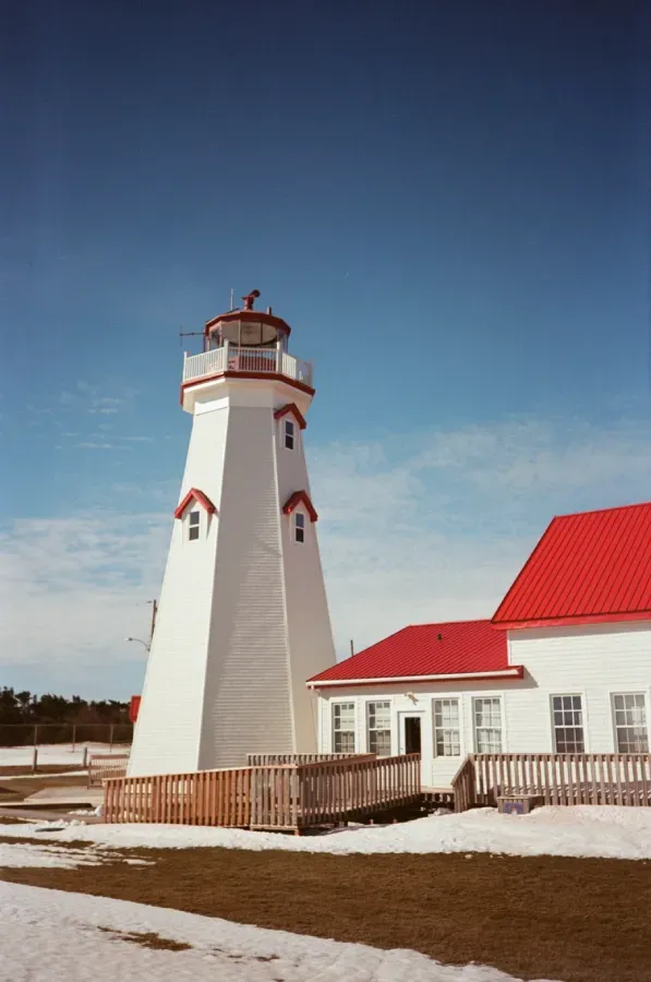 East Point lighthouse with red trim stands next to a white building with a red roof on a snowy day.