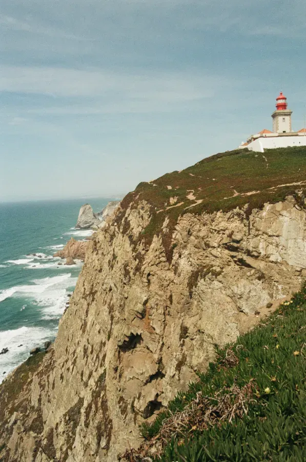 A film photo of the Farol do Cabo da Roca lighthouse on a cliff from afar
