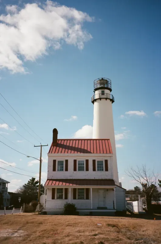 Fenwick Island lighthouse with a red roof stands next to a matching two-story keeper’s house under a blue sky