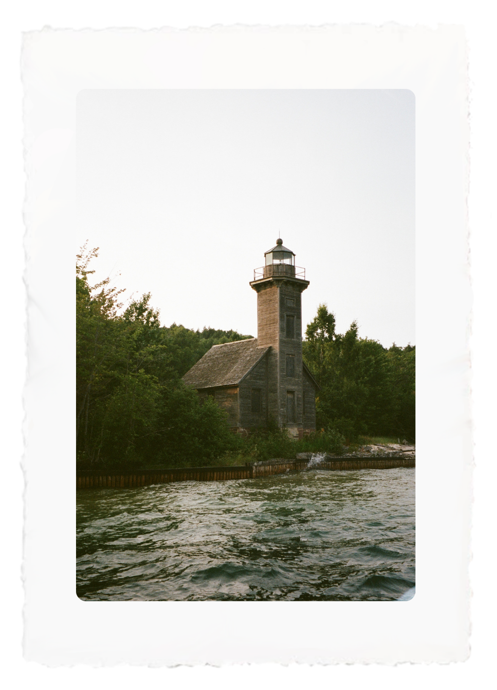 Stone lighthouse beside trees on a rocky shoreline at dusk