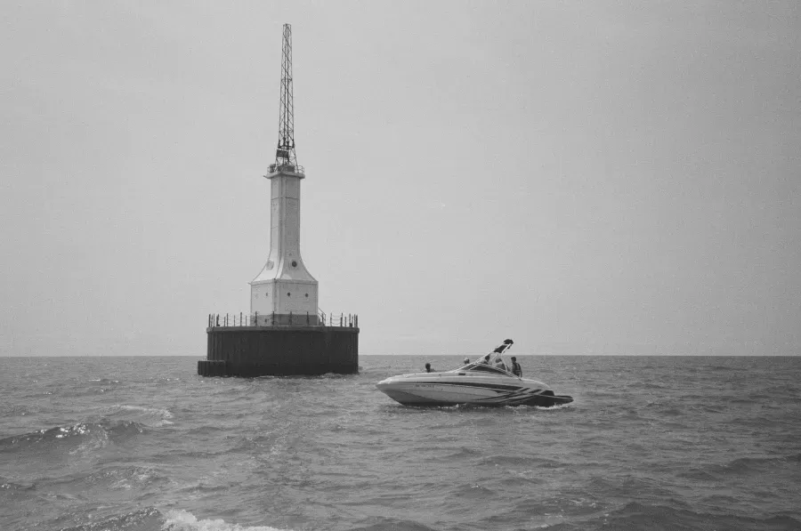 A boat sails near Gravelly Shoal lighthouse with a tall tower in the ocean under a cloudy sky.