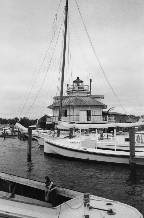 Hooper Strait Lighthouse on stilts in water, docked sailboat in foreground, cloudy sky.