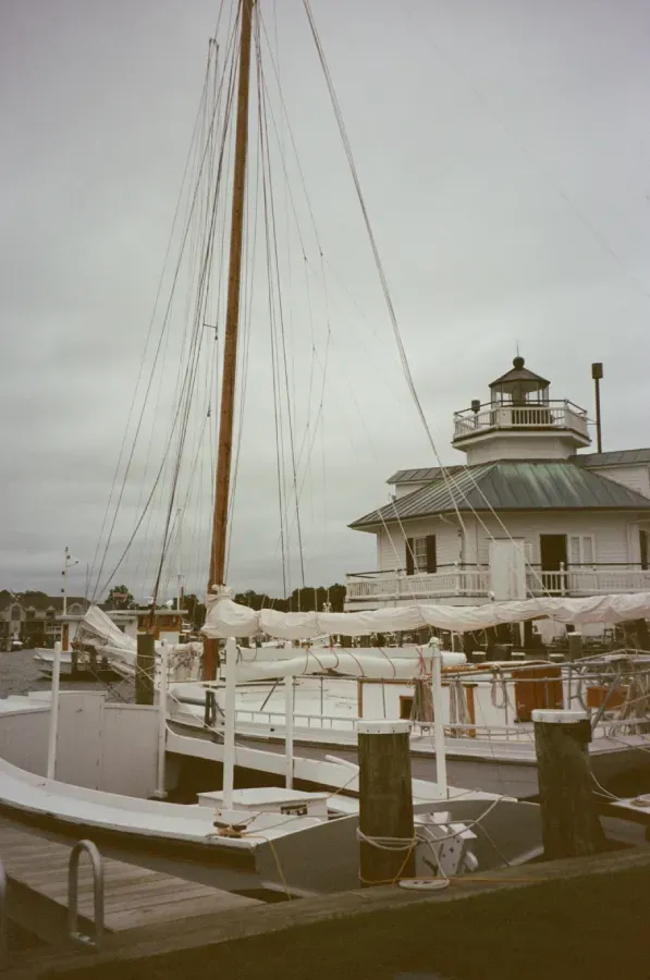 White boat docked near a white building with a lighthouse on top, cloudy sky.