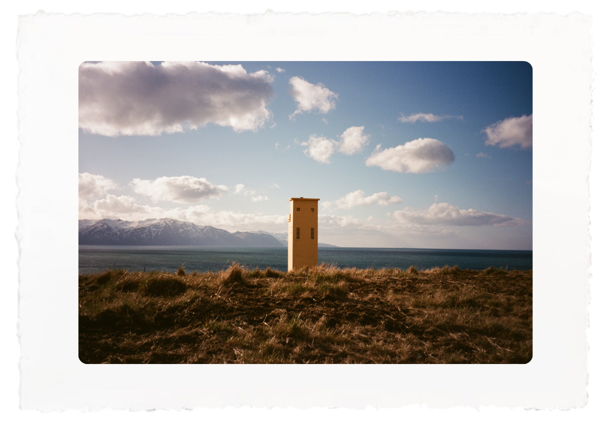 Single stone tower in a grassy field with mountains and a cloudy sky in the distance