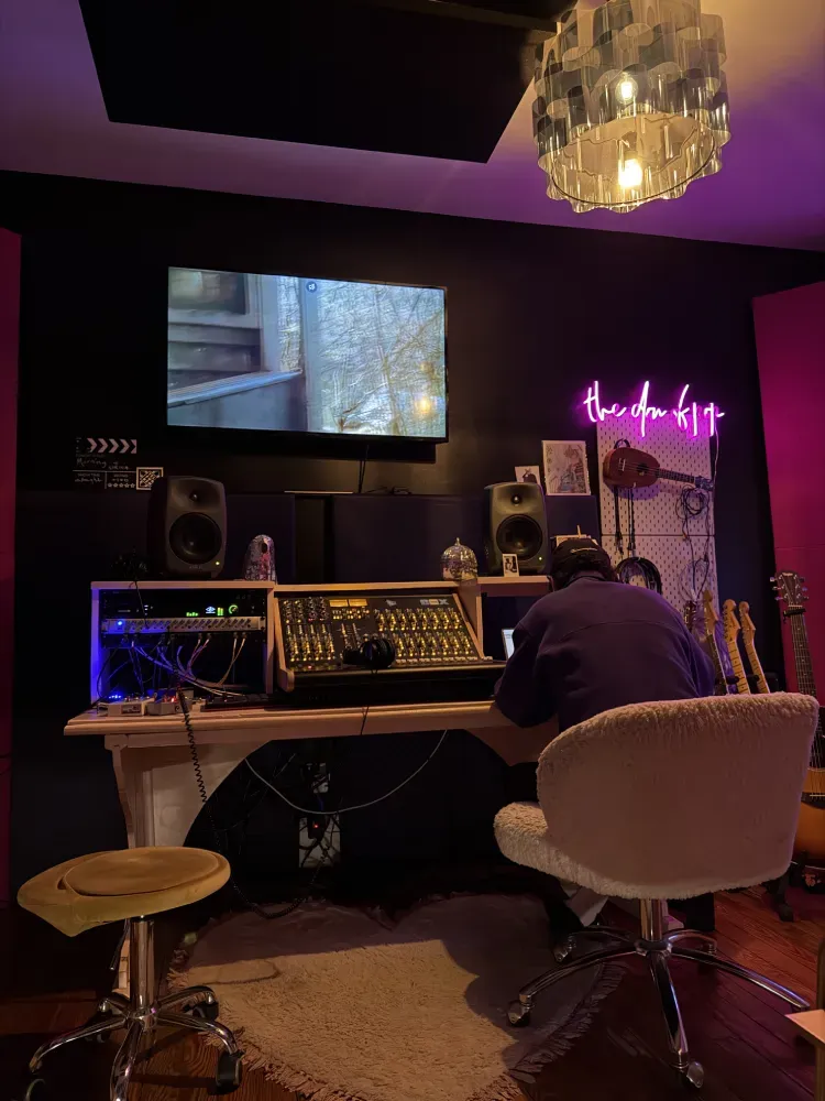 Lawrence from Don of Pop Studios seated at a mixing desk under magenta neon lights.