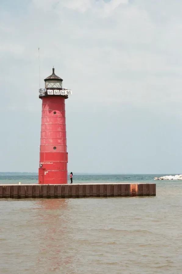 Kenosha Pierhead lighthouse on a pier, with a person standing near it, against a cloudy sky.