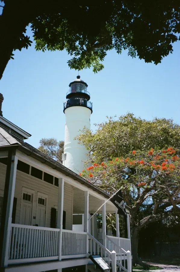 Key West lighthouse and adjacent house with a porch; trees frame the view under a blue sky.