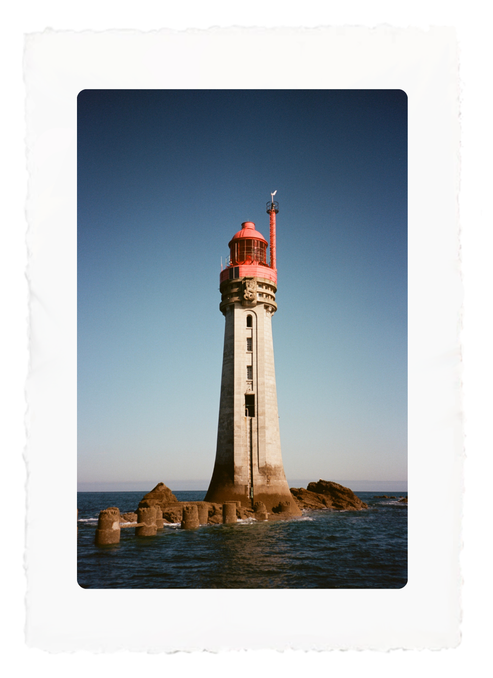 Lighthouse on a rocky islet under a clear blue sky, with waves around its base.