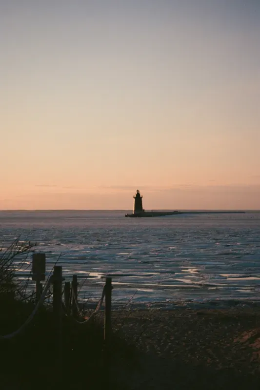 Lewes lighthouse stands on a breakwater in the distance, viewed from a sandy shore at sunset over the sea
