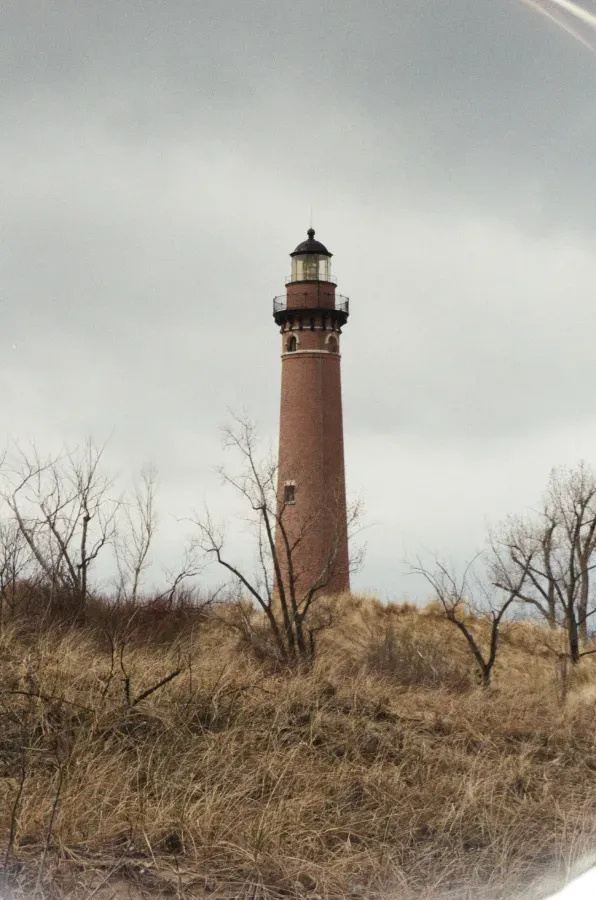 Film photograph of Little Sable Point lighthouse on a grassy dune under a cloudy sky.