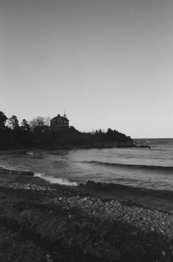 Black and white photo of Marquette Portrait on a rocky cliff overlooking a wavy ocean.