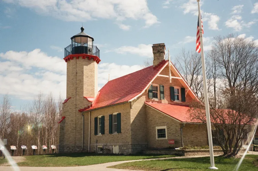 McGulpin Point Lighthouse with red roof and an American flag on a sunny day.