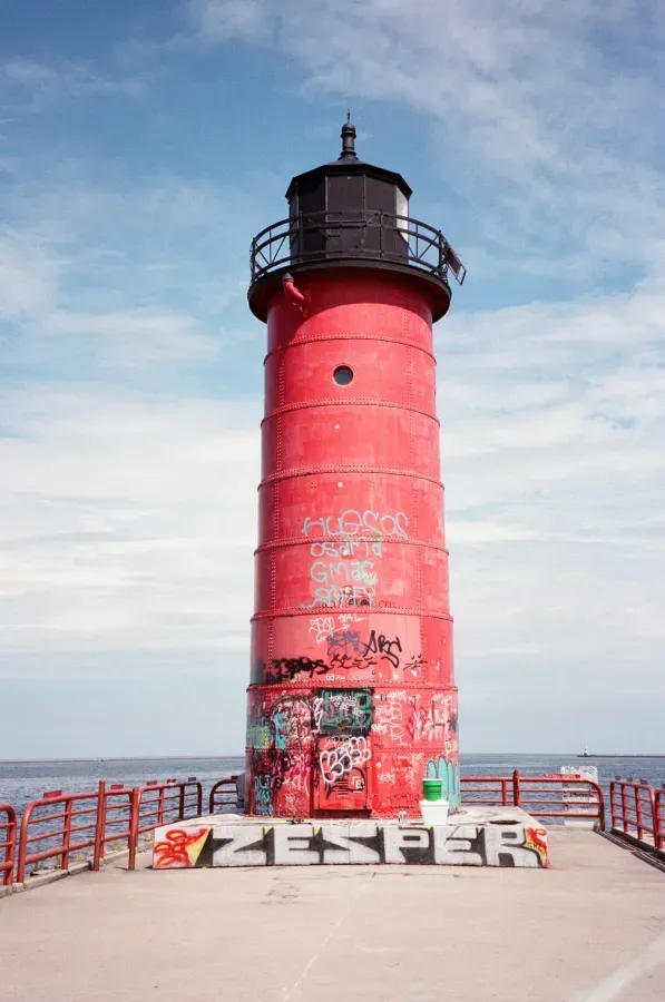Milwaukee Pierhead Red lighthouse on a pier, with graffiti, under a blue sky.