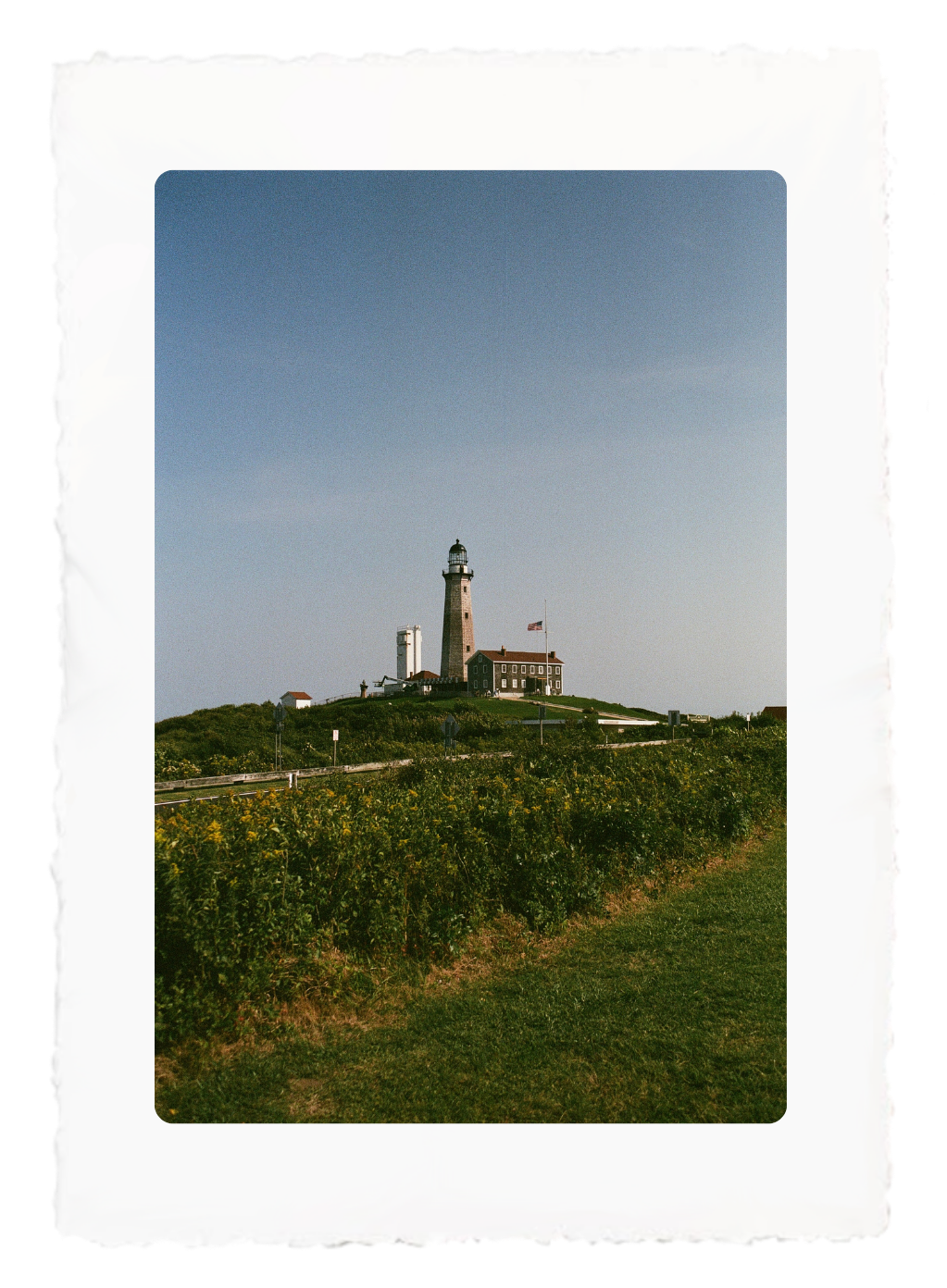 Lighthouse on a grassy hill under a clear blue sky with a small building beside it