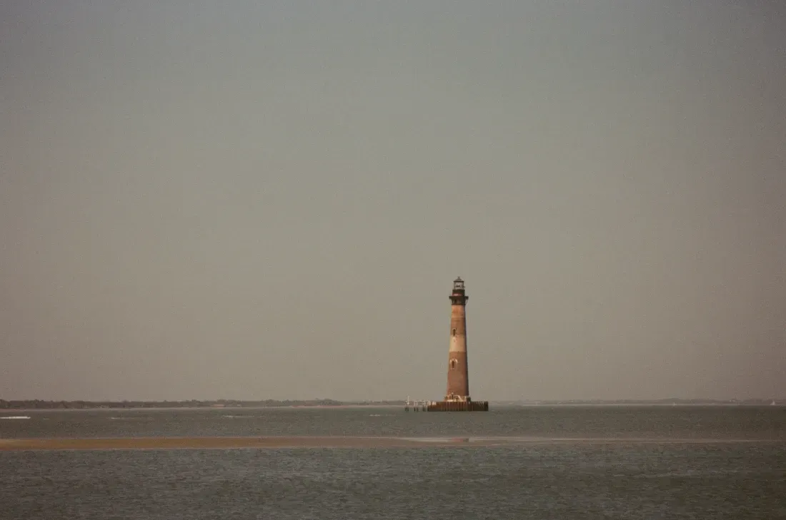 Distant photo of Morris Island lighthouse on a calm sea under a hazy sky