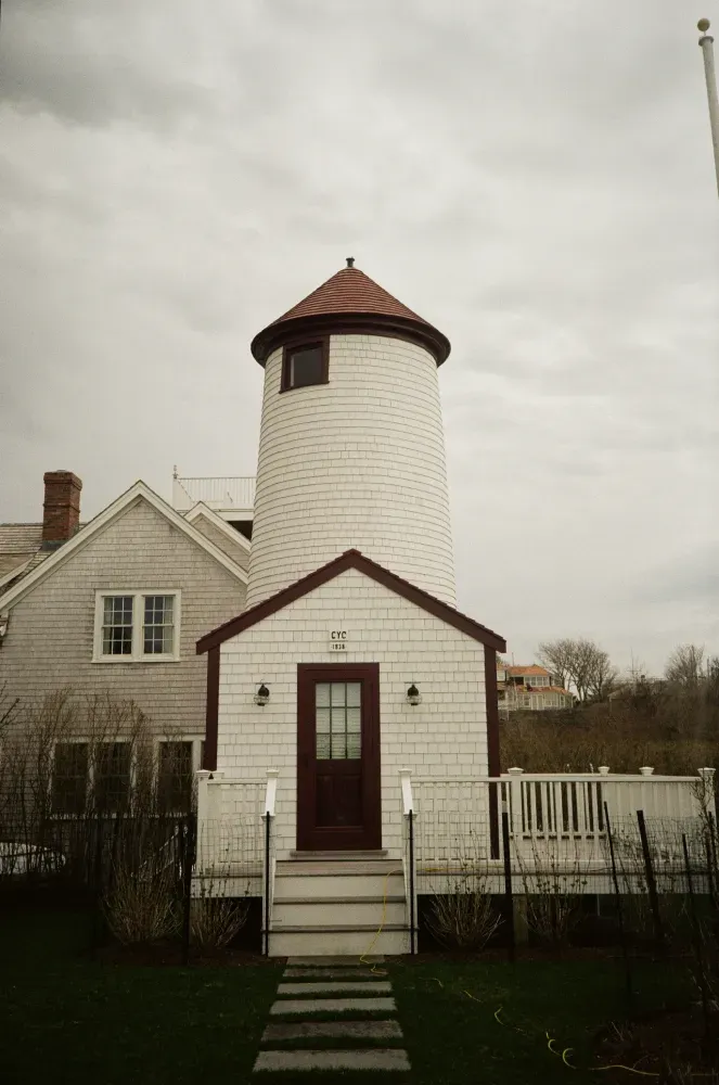 Film photo of Nantucket Cliff Range lighthouse set beside a house and fence under a cloudy sky