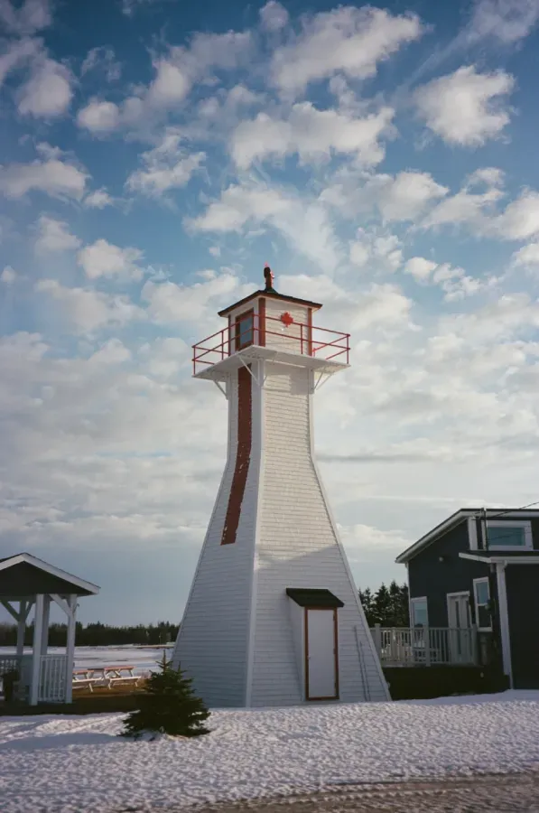 Northport Range Rear lighthouse with red accents stands on snow-covered ground under a bright, cloudy blue sky
