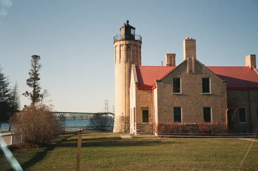 Old Mackinac lighthouse with red roof, tower, and grassy yard under blue sky.